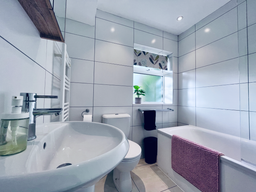 Tiled bathroom in white with pink bath rug and black hand towels.