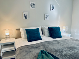 Hotel styled double bed with white linen, blue velvet cushions, grey throw, bedside table and lamps. 